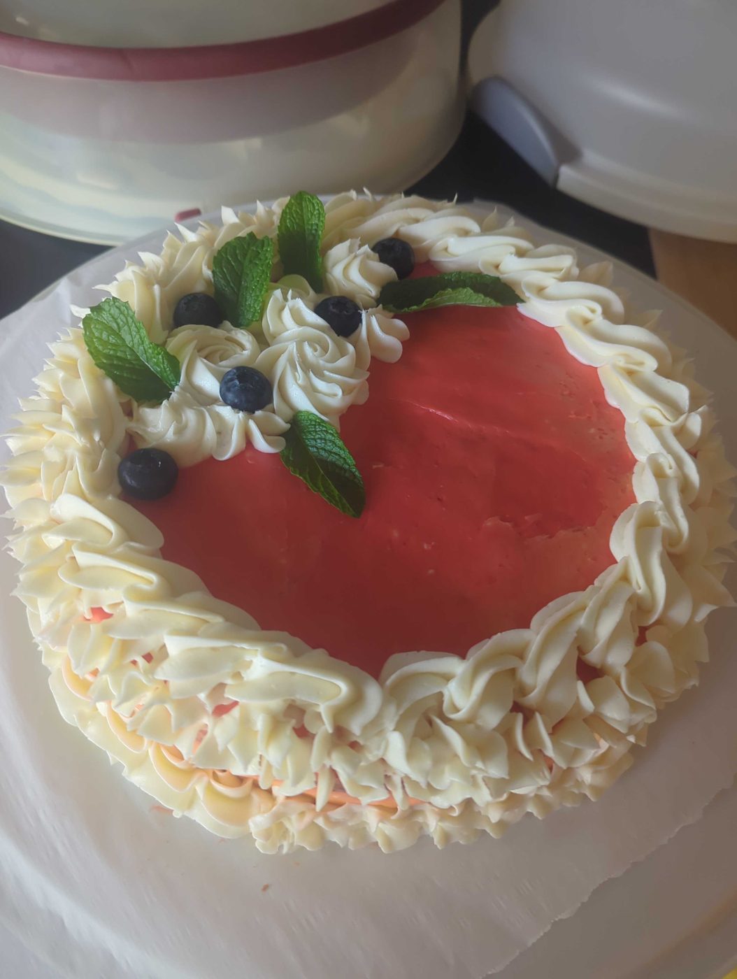 Red-glazed cake ringed with piped frosting, blueberries, and mint