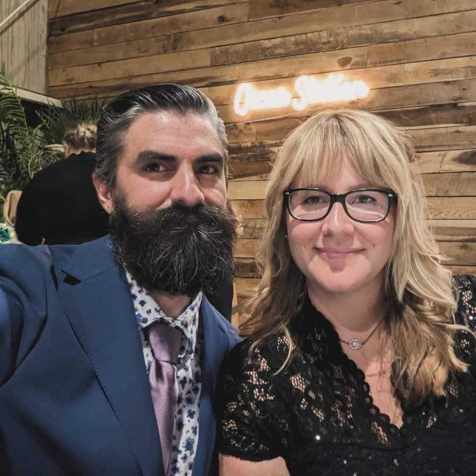 Julee and her fiancé at an event, smiling in front of a wood-paneled wall